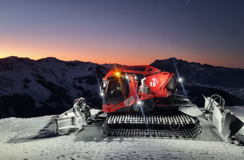 Red snow groomer on snowy mountain ridge at sunset, surrounded by alpine mountain scenery | © Hochkönig Bergbahnen GmbH