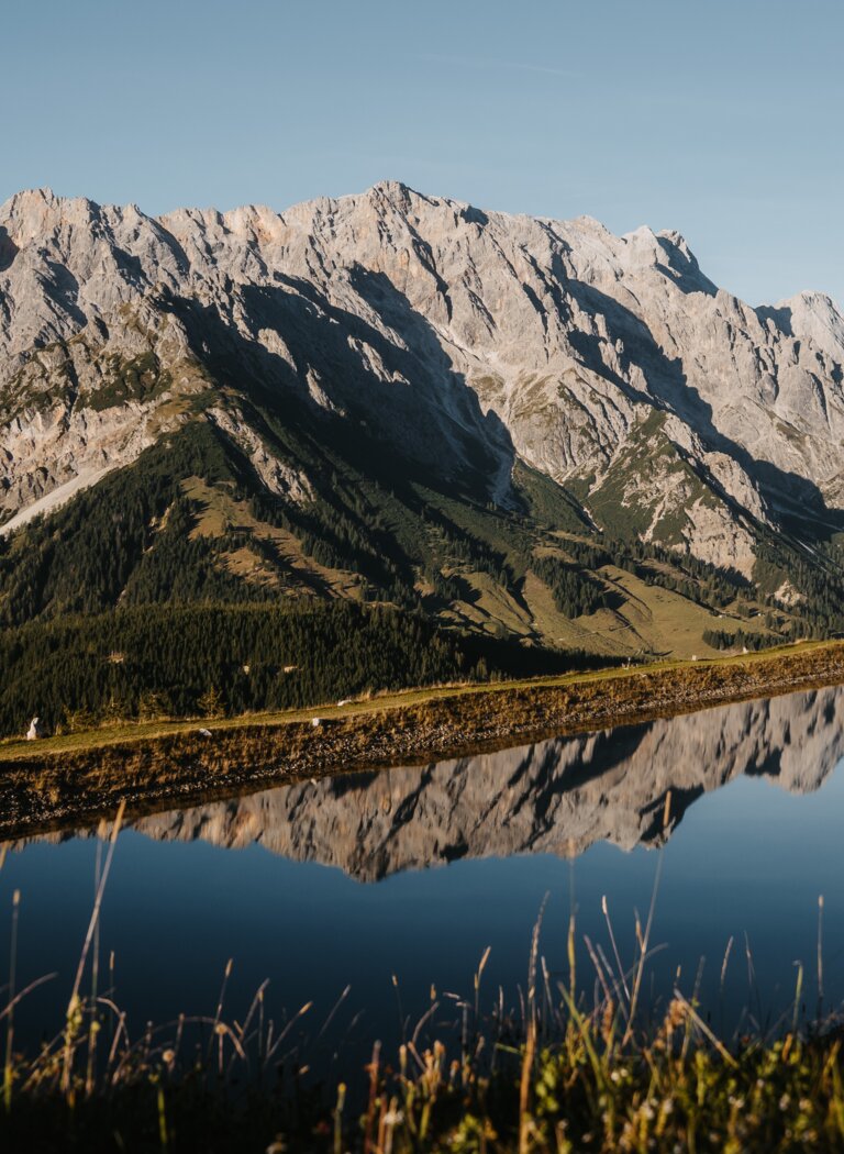 Rocky mountain massif reflected in calm Alpine lake under a clear sky in mountain landscape | © Hochkönig Bergbahnen GmbH