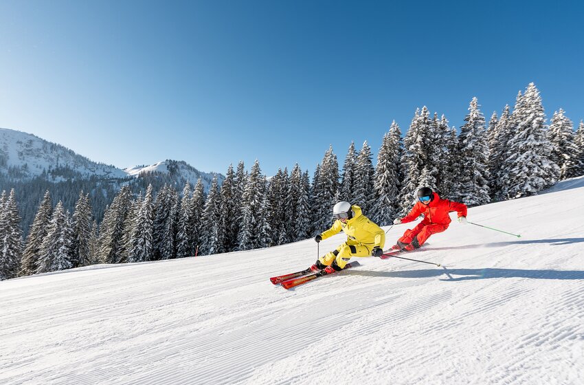 Two skiers carving in colorful suits on a perfectly groomed slope at Hochkönig.  | © Hochkönig Bergbahnen GmbH