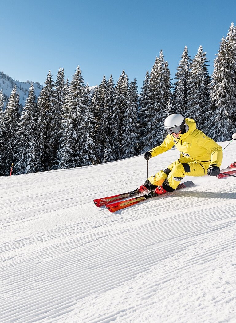 Two skiers carving in sync on a freshly groomed slope in Hochkönig, wearing bright ski suits. | © Hochkönig Bergbahnen GmbH