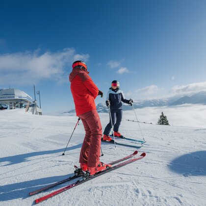 Zwei Skifahrer stehen auf präparierter Piste nahe einer Bergstation, Nebel liegt im Tal vor Alpenpanorama | © Ski amadé GmbH